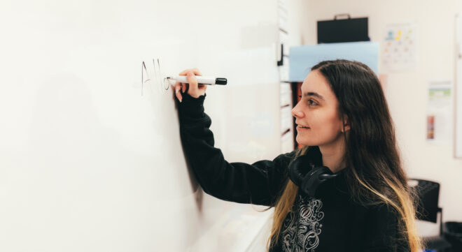 Jeune étudiante qui fréquente un milieu adapté de scolarisation qui écrit au tableau dans une classe